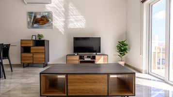 Un soggiorno moderno con una TV a schermo piatto, arredi in legno e una grande finestra con vista sulla città.
