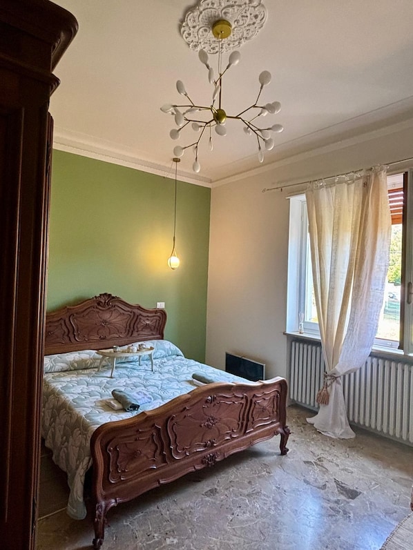 Een slaapkamer met een houten bed, een plafondlamp, een radiator en een raam met gordijnen.