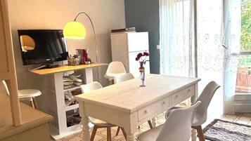 Ein Essbereich mit einem weißen Tisch, vier Stühlen, einem Fernseher und einer Lampe.