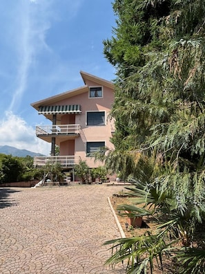 Um edifício de dois andares com varanda e entrada por um caminho pavimentado.