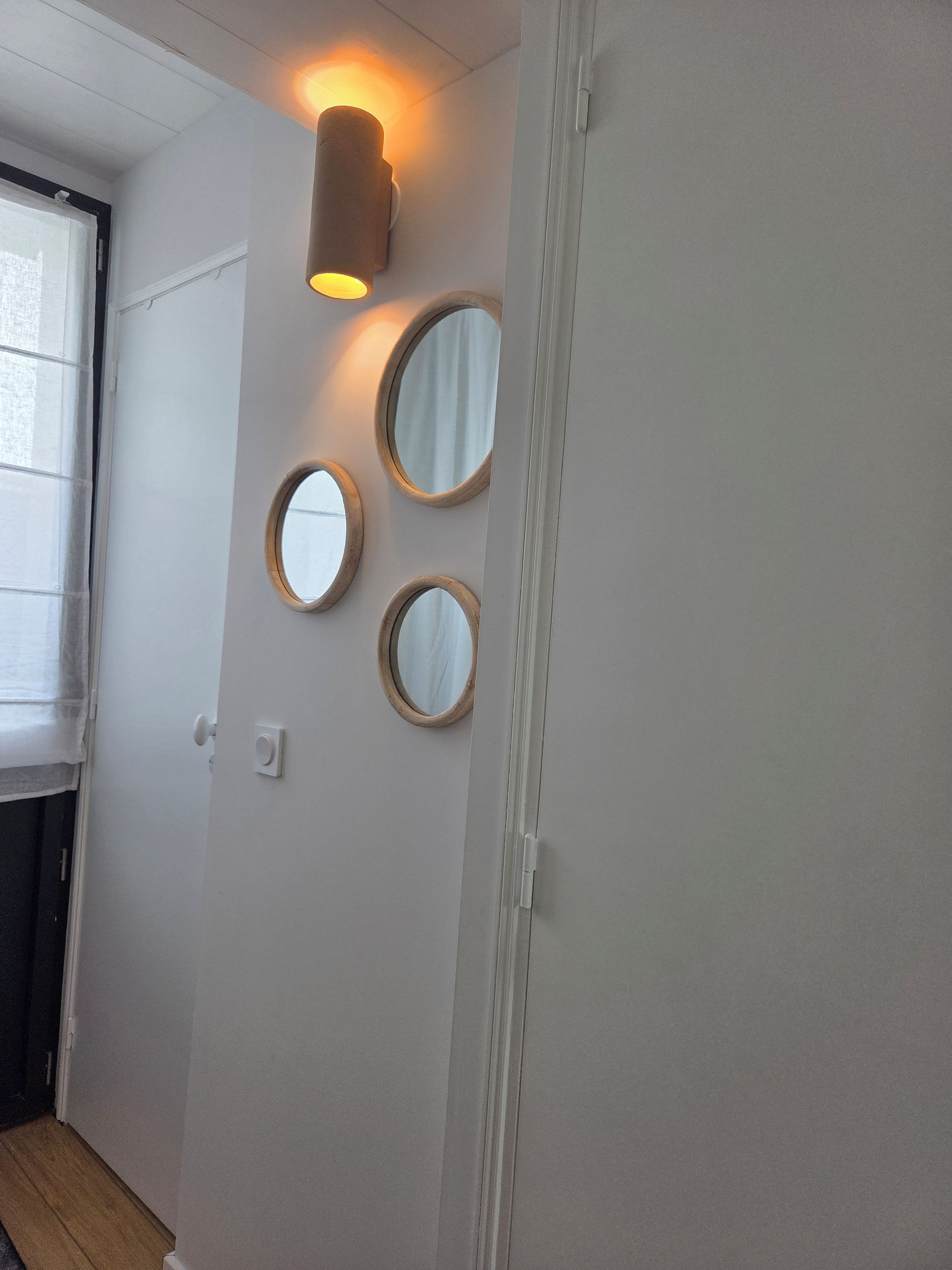A hallway with a door, a light fixture, and three wall-mounted mirrors.