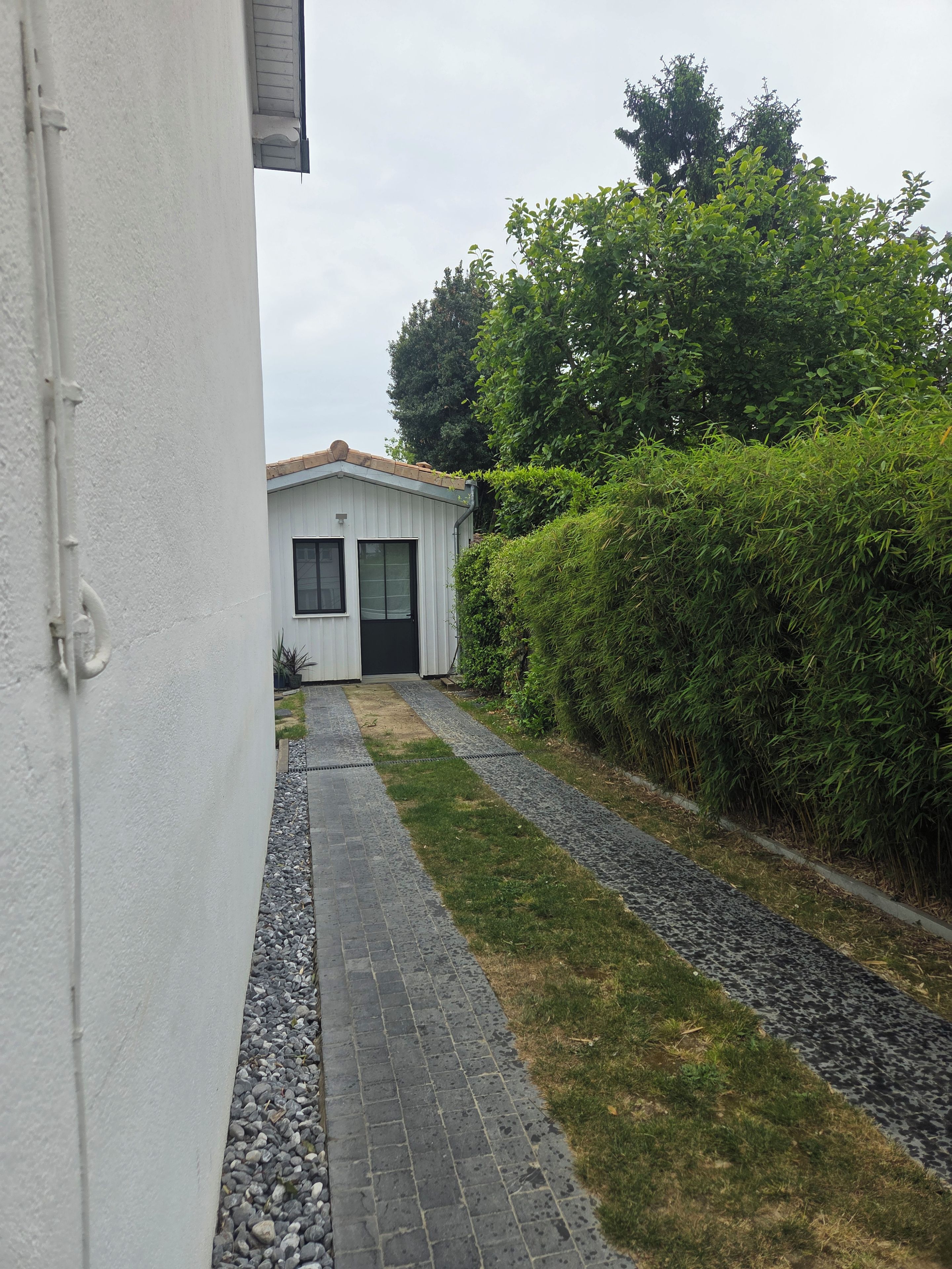 A pathway leading to a white building with a door and windows, surrounded by greenery and a gravel path.