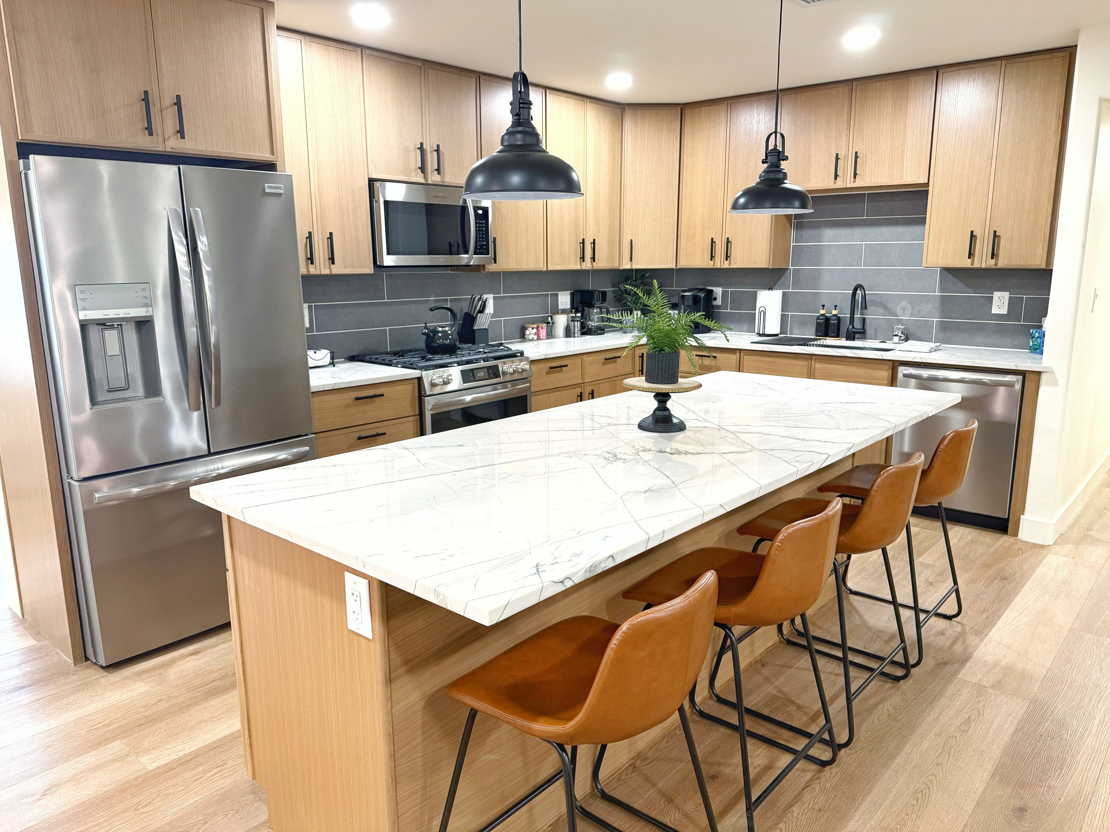 Een moderne keuken met roestvrijstalen apparatuur, houten kastjes, een marmeren eiland en barstoelen.