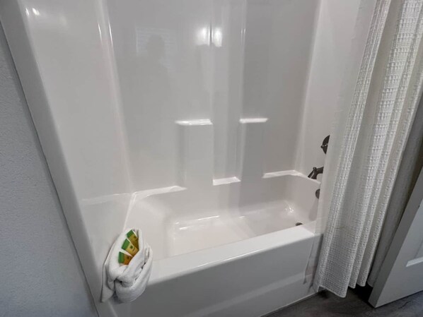 Une baignoire blanche avec un rideau de douche, un porte-serviettes avec une serviette et un pommeau de douche.