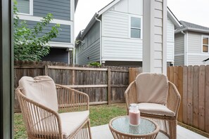 Eine Terrasse mit Korbstühlen, einem Glastisch, einem Holzzaun und einem Haus im Hintergrund.