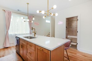 Una cocina moderna con una isla central, pileta de acero inoxidable e iluminación colgante.