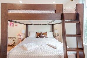 Una cama litera con estructura de madera, ropa de cama blanca y una escalera. Hay mesitas de noche con lámparas y un pequeño marco de fotos a la izquierda.