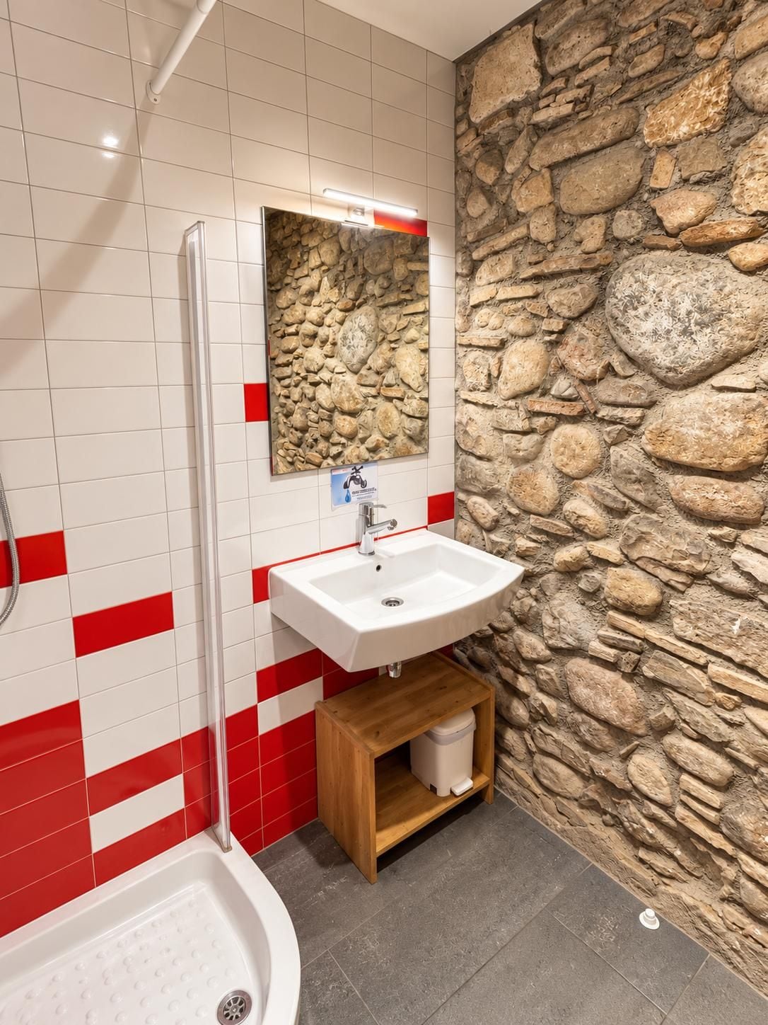 Un baño con pared de piedra, un lavabo blanco, un espejo y una ducha.