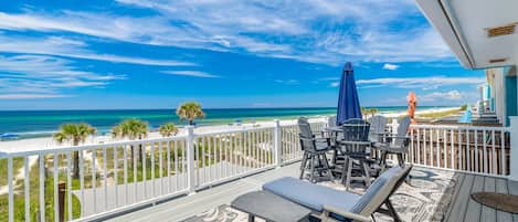 A deck with a view of the ocean, outdoor furniture, and a white fence.