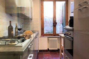 Una cucina con piano cottura a gas, forno e una finestra che dà su un muro in mattoni.