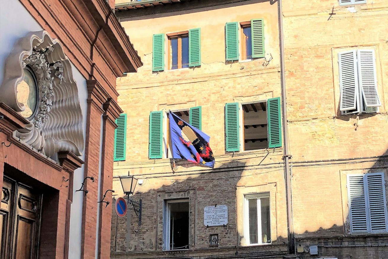A building with multiple windows, some with shutters, and a flag hanging between two windows.
