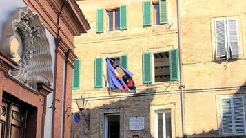 A building with multiple windows, some with shutters, and a flag hanging between two windows.