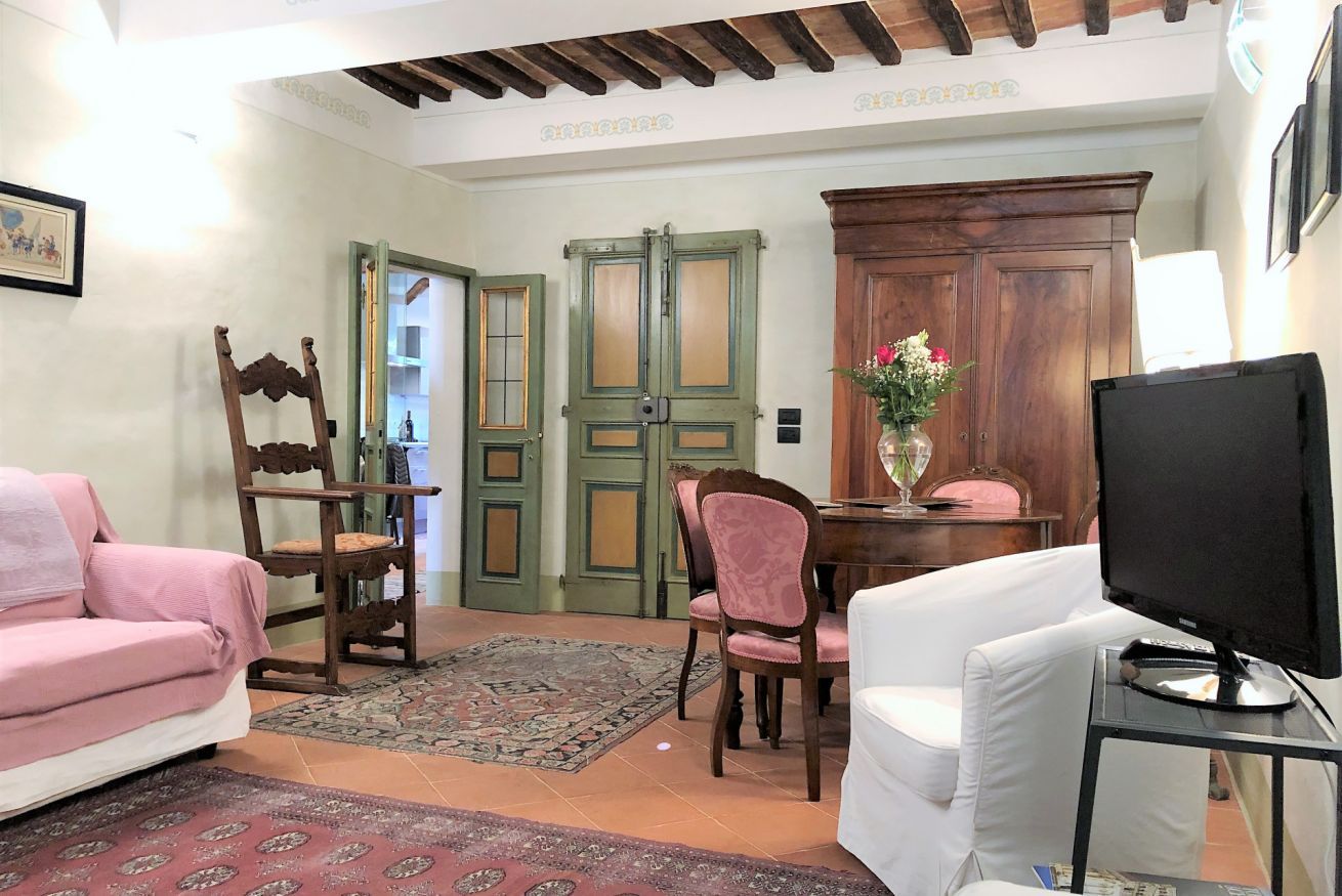 A living room with a sofa, a TV, a dining table with chairs, a wooden cabinet, and a door with glass panels.