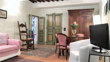 A living room with a sofa, a TV, a dining table with chairs, a wooden cabinet, and a door with glass panels.
