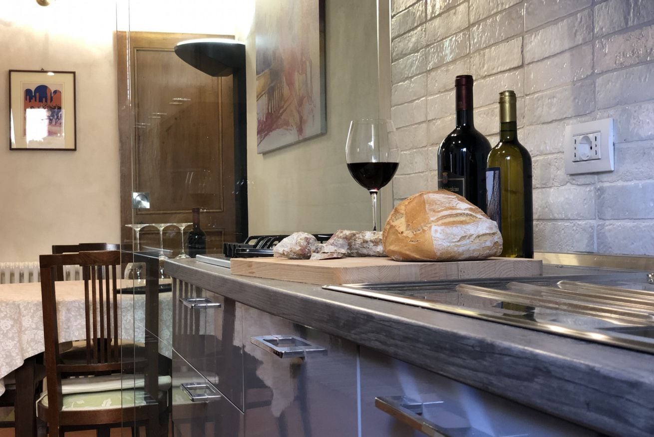 A modern kitchen with a marble countertop, a loaf of bread, two wine bottles, and a glass of red wine.