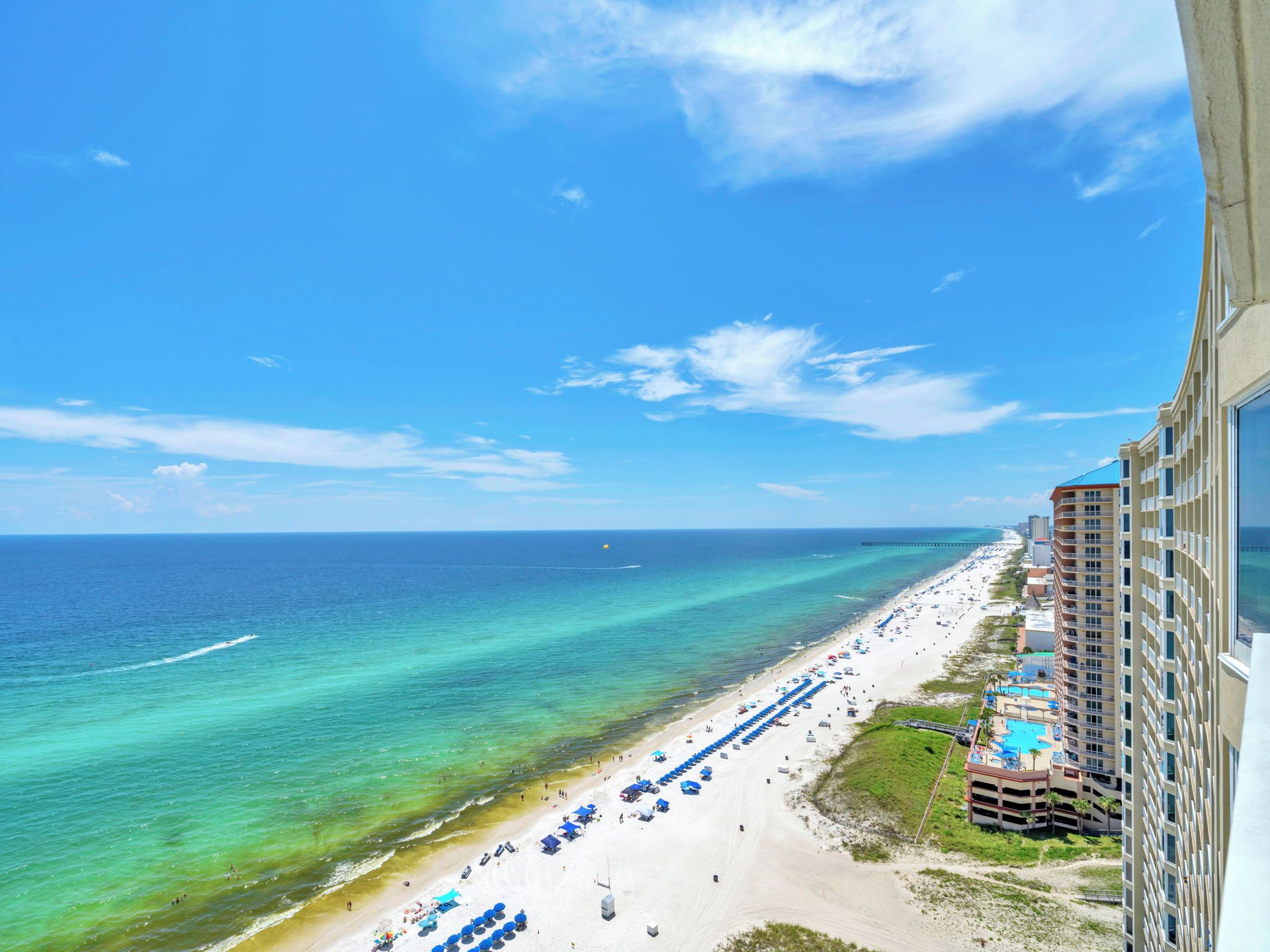 A beachfront hotel with a long sandy beach, a clear blue ocean, and a pier in the distance.