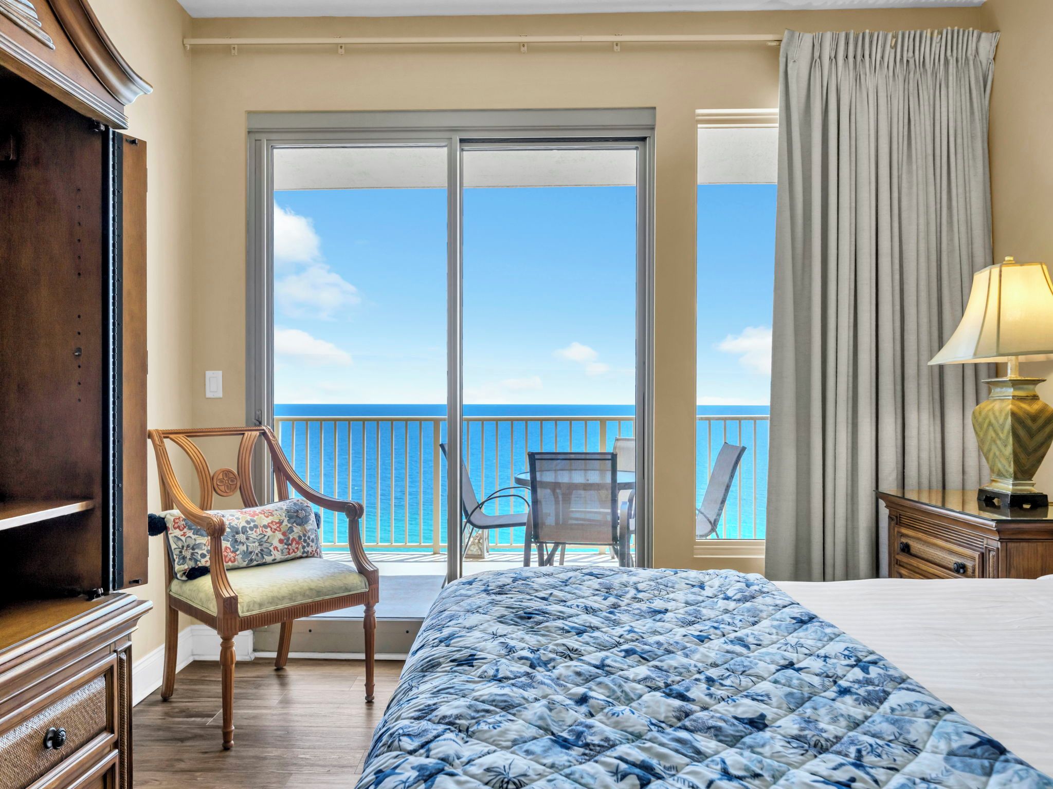 Hotelkamer met een groot bed, een stoel, een tafel en uitzicht op de oceaan door een schuifdeur.