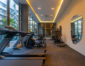 A gym with treadmills, exercise equipment, and a view of a building through large windows. - Acqualina Resort By Day by Day (JOÃO PESSOA)