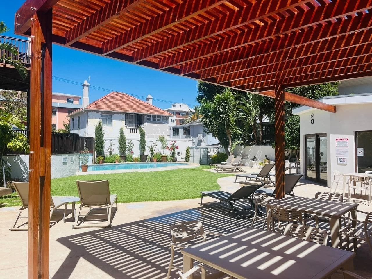 Une terrasse extérieure avec des tables et des chaises, une piscine et un bâtiment en arrière-plan.