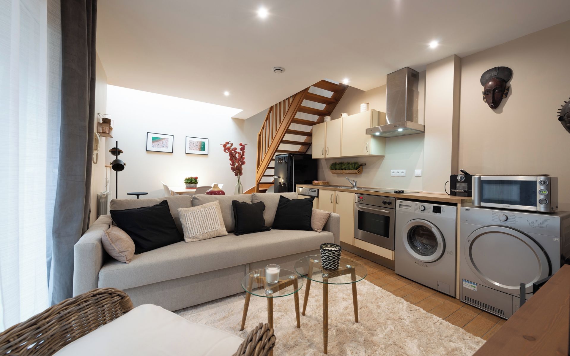 A compact living space with a sofa, a dining table, a kitchen area with appliances, and a staircase.