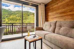 Una habitació amb un sofà, una taula petita i vista a un paisatge de muntanyes a través d'una finestra gran.