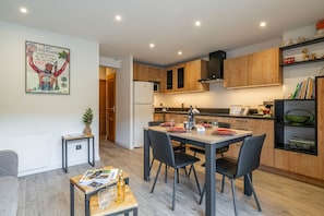 A modern kitchen with wooden cabinets, a built-in microwave, and a dining area with a table set for two. - Perce Neige - Proche piste olympique Luc (Saint-Chaffrey)