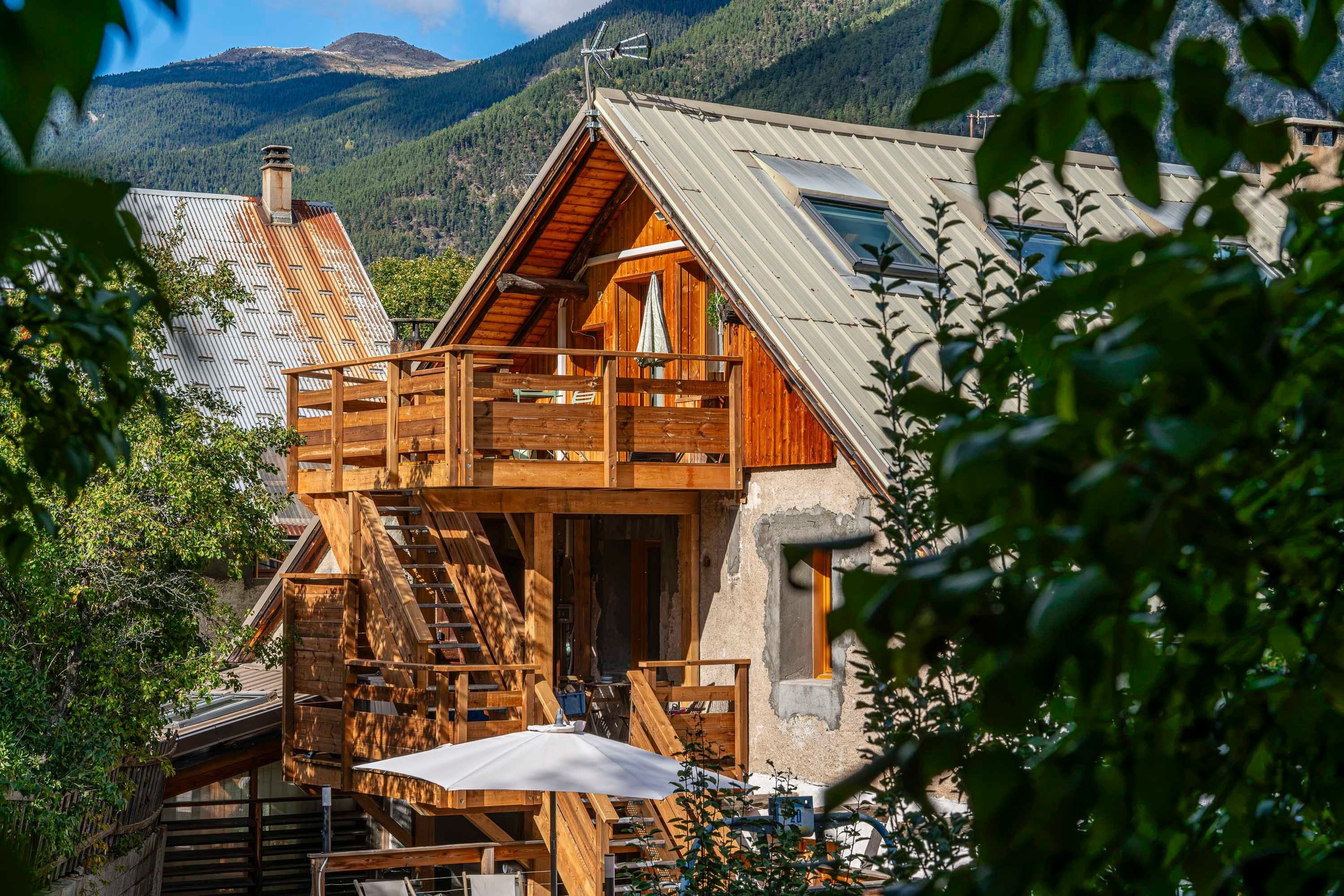 A wooden chalet with a balcony, a staircase, and a view of a mountainous landscape.