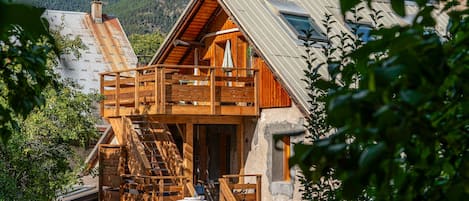 A wooden chalet with a balcony, a staircase, and a view of a mountainous landscape.