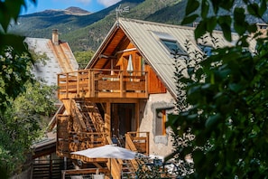 Un chalé de madera con balcón, una escalera y vistas a un paisaje montañoso.
