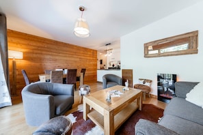 Una sala de estar moderna con una pared de madera, una chimenea y una zona de comedor con una mesa y sillas de madera.