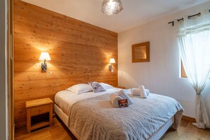 Ein Schlafzimmer mit einem Holz-Kopfteil, zwei Nachttischlampen, einem Bett mit weißer Bettwäsche, einem kleinen Nachttisch und einem Fenster mit Vorhängen.