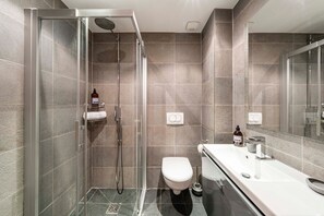 Un baño moderno con ducha acristalada, inodoro y lavamanos con espejo.