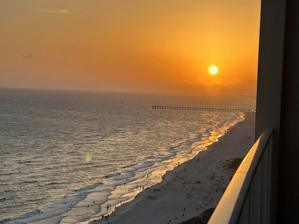A beach with a pier extending into the water, viewed from a balcony.