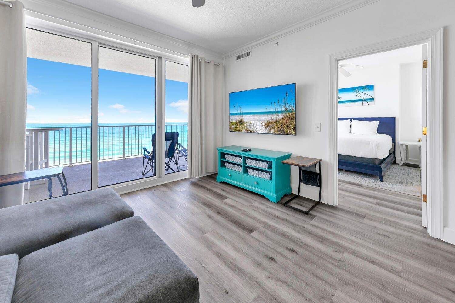 Une chambre d’hôtel moderne dotée d’un balcon, d’une grande fenêtre, d’un lit, d’un bureau et d’un meuble de rangement de couleur turquoise.