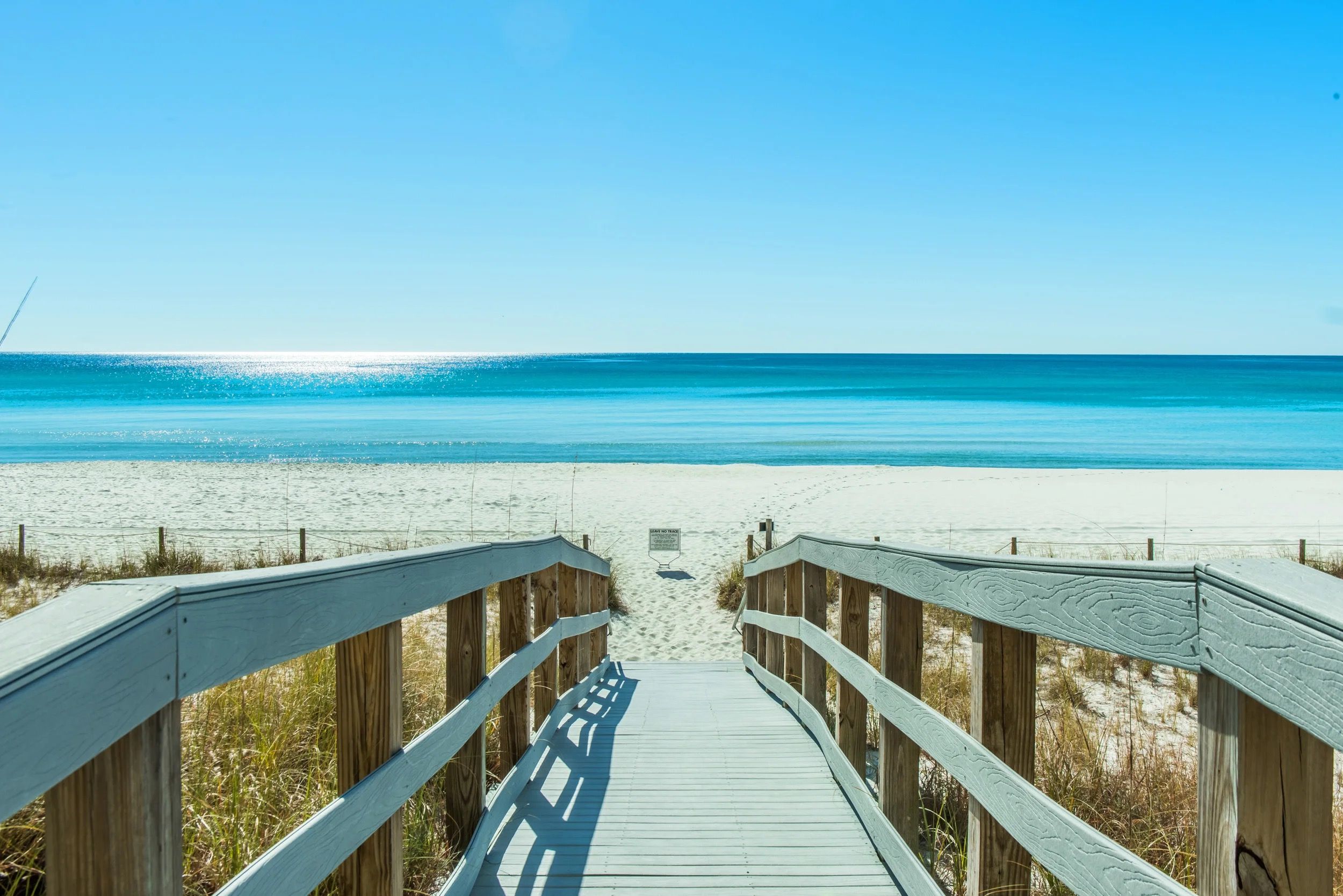 A wooden boardwalk leading to a beach with a clear view of the ocean.