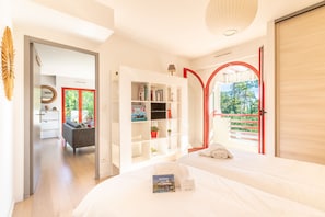 A modern bedroom with a large bed, a built-in bookshelf, and a view of the outdoors through a red-framed window. - Terrazza - Double terrasse lac d'Hossegor (Hossegor)