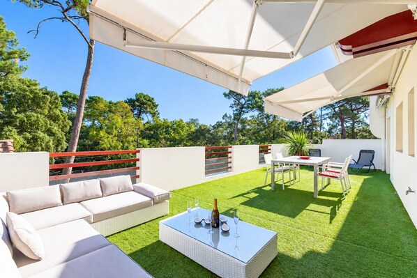 A patio with a white sofa, a glass-top coffee table, and a dining table with chairs. - Terrazza - Double terrasse lac d'Hossegor (Hossegor)
