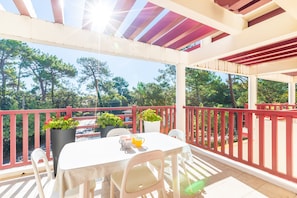 A covered outdoor seating area with a table and chairs, surrounded by a red railing, overlooking a forested area. - Terrazza - Double terrasse lac d'Hossegor (Hossegor)