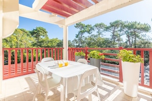 A covered outdoor patio with a table and chairs, surrounded by a red railing, and potted plants. - Terrazza - Double terrasse lac d'Hossegor (Hossegor)