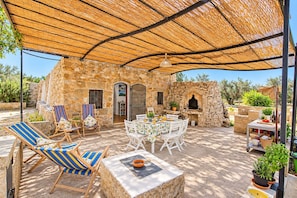 Une terrasse extérieure avec des murs en pierre, une table dressée pour le repas et un espace barbecue.