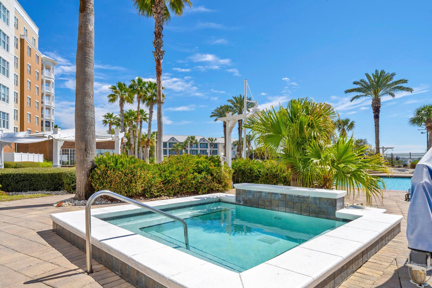 A swimming pool with a white deck, surrounded by palm trees and a building with balconies.