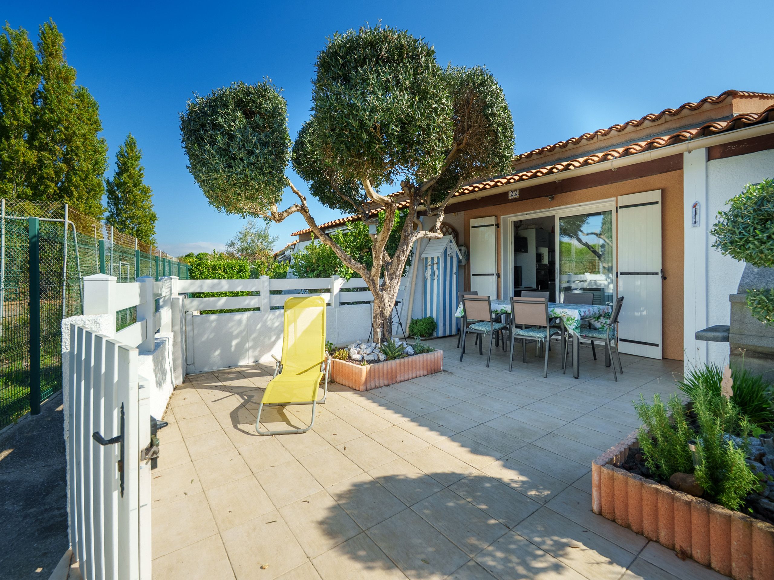 A patio area with a dining table and chairs, a yellow chair, and a white fence.