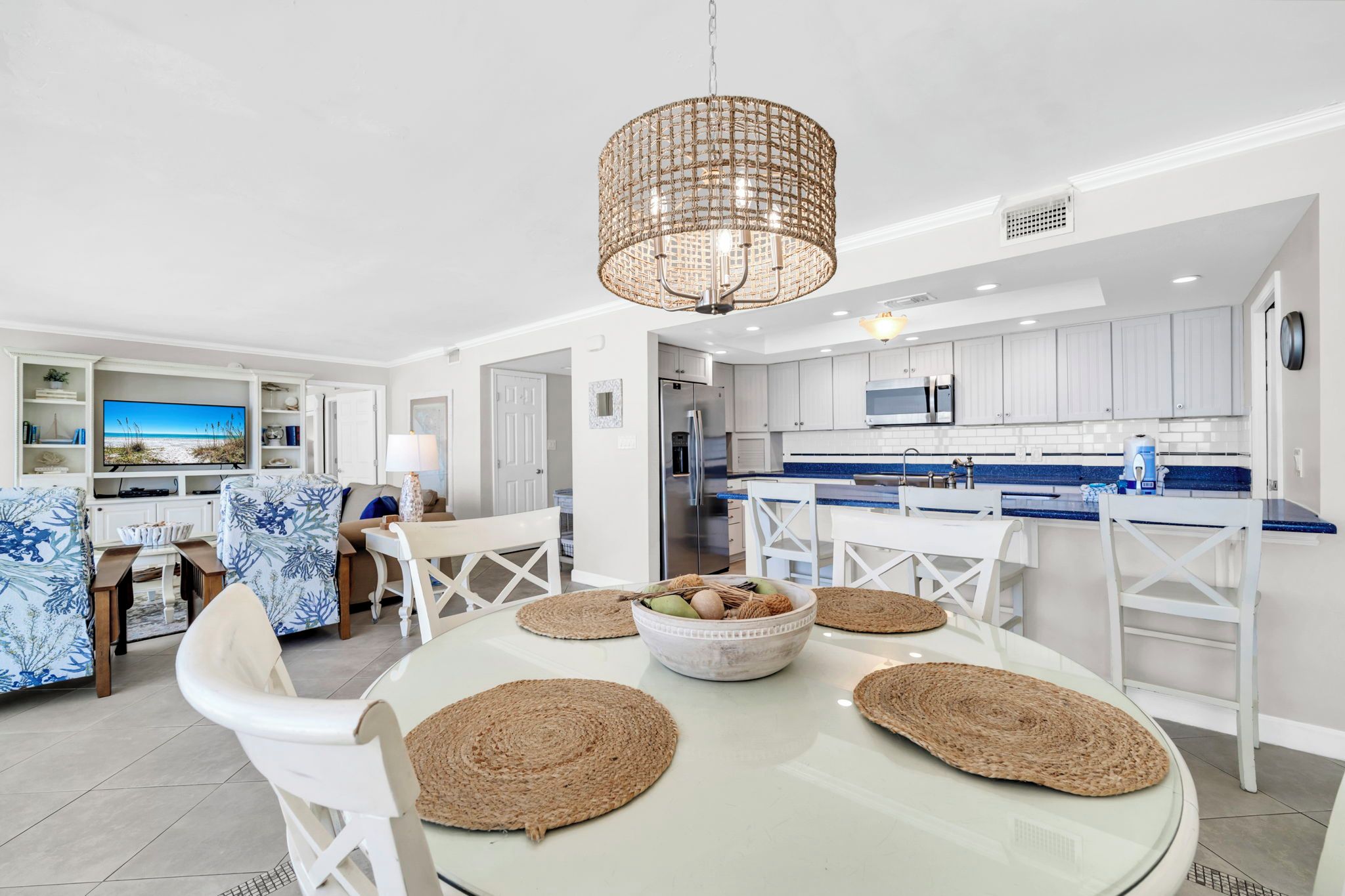 A modern kitchen with white cabinets, a blue countertop, and a dining area with white chairs and a glass table.