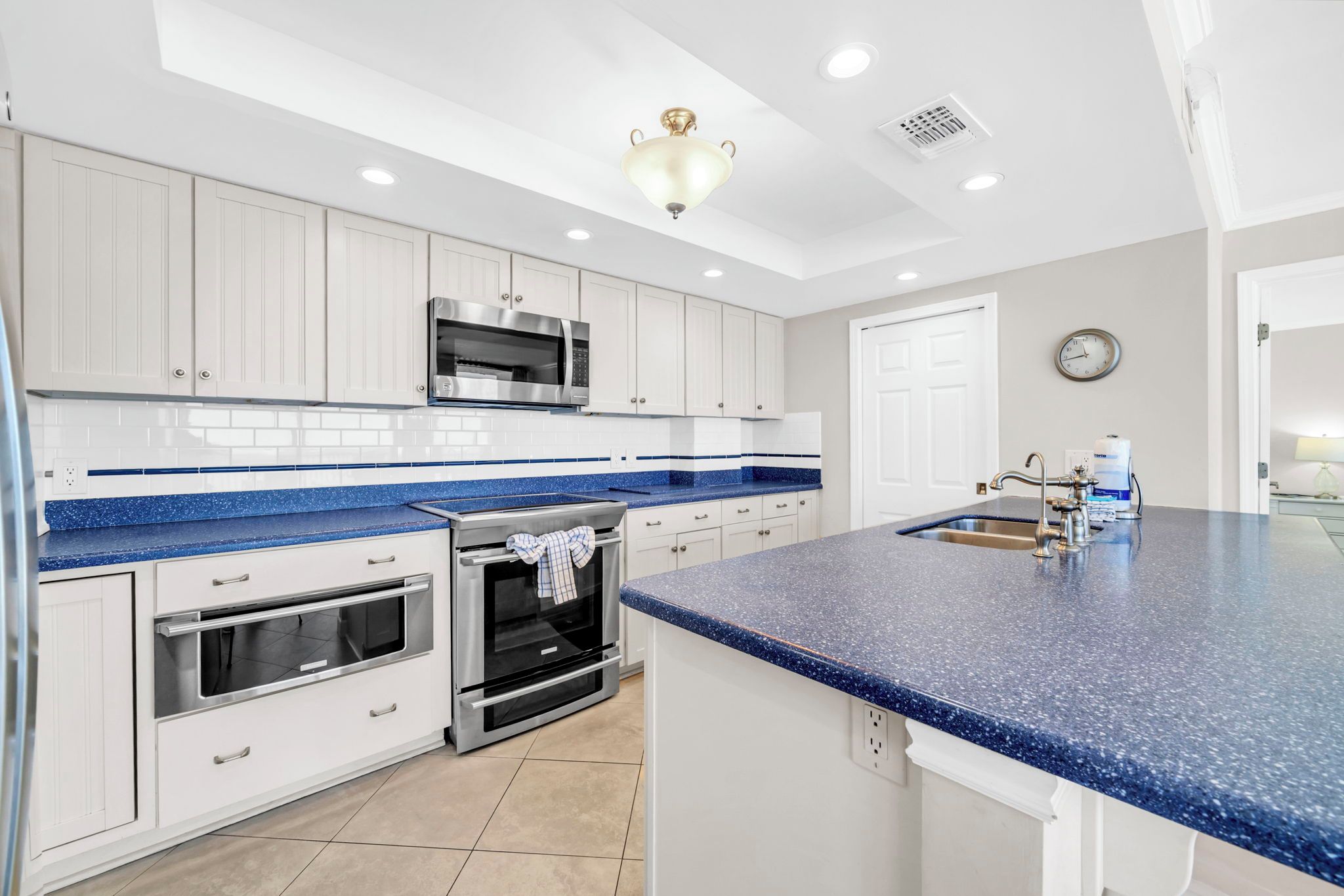 A modern kitchen with white cabinets, a blue granite countertop, stainless steel appliances, and a central island with a sink.