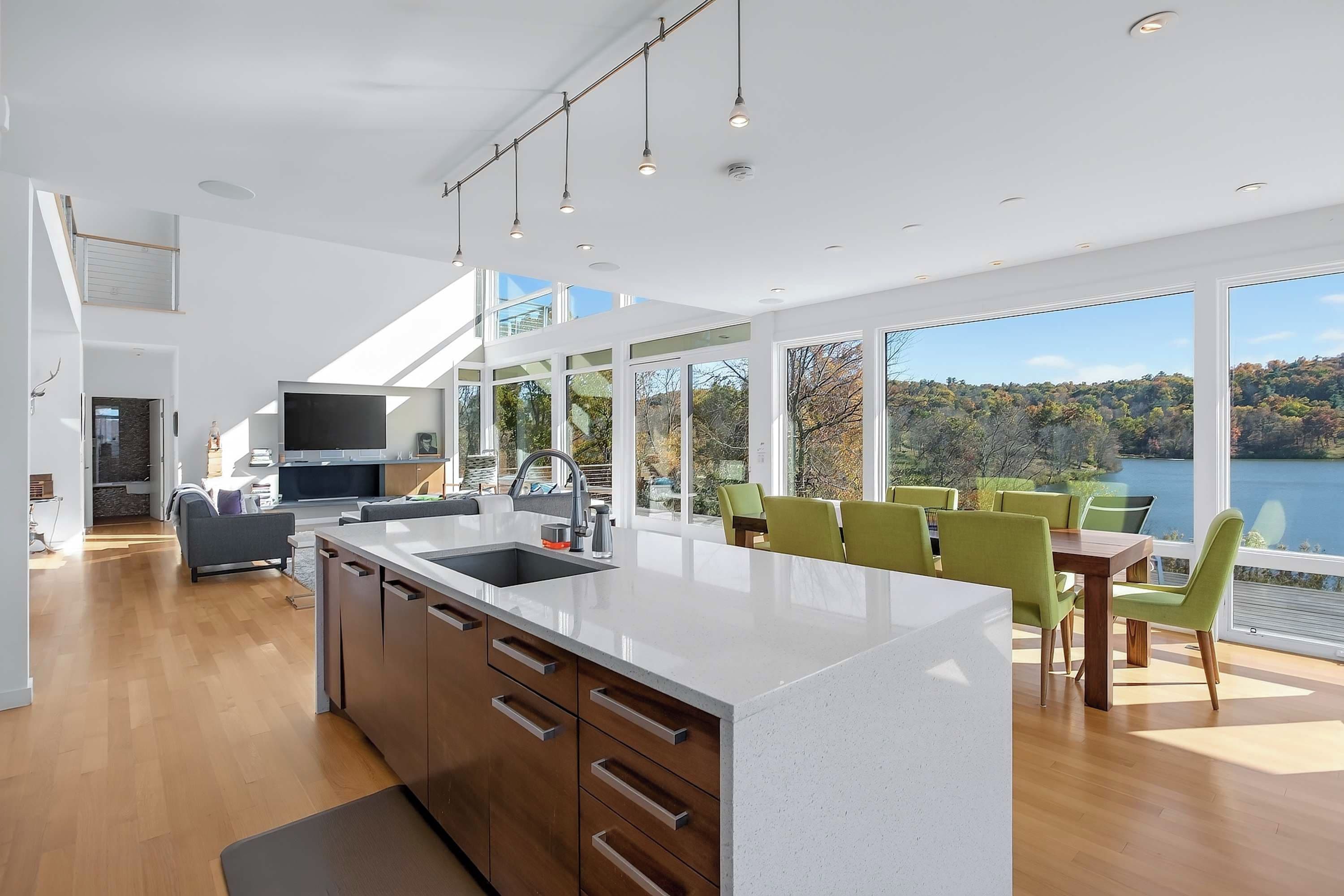 A modern kitchen with a large island, dining area with green chairs, and a view of a lake.