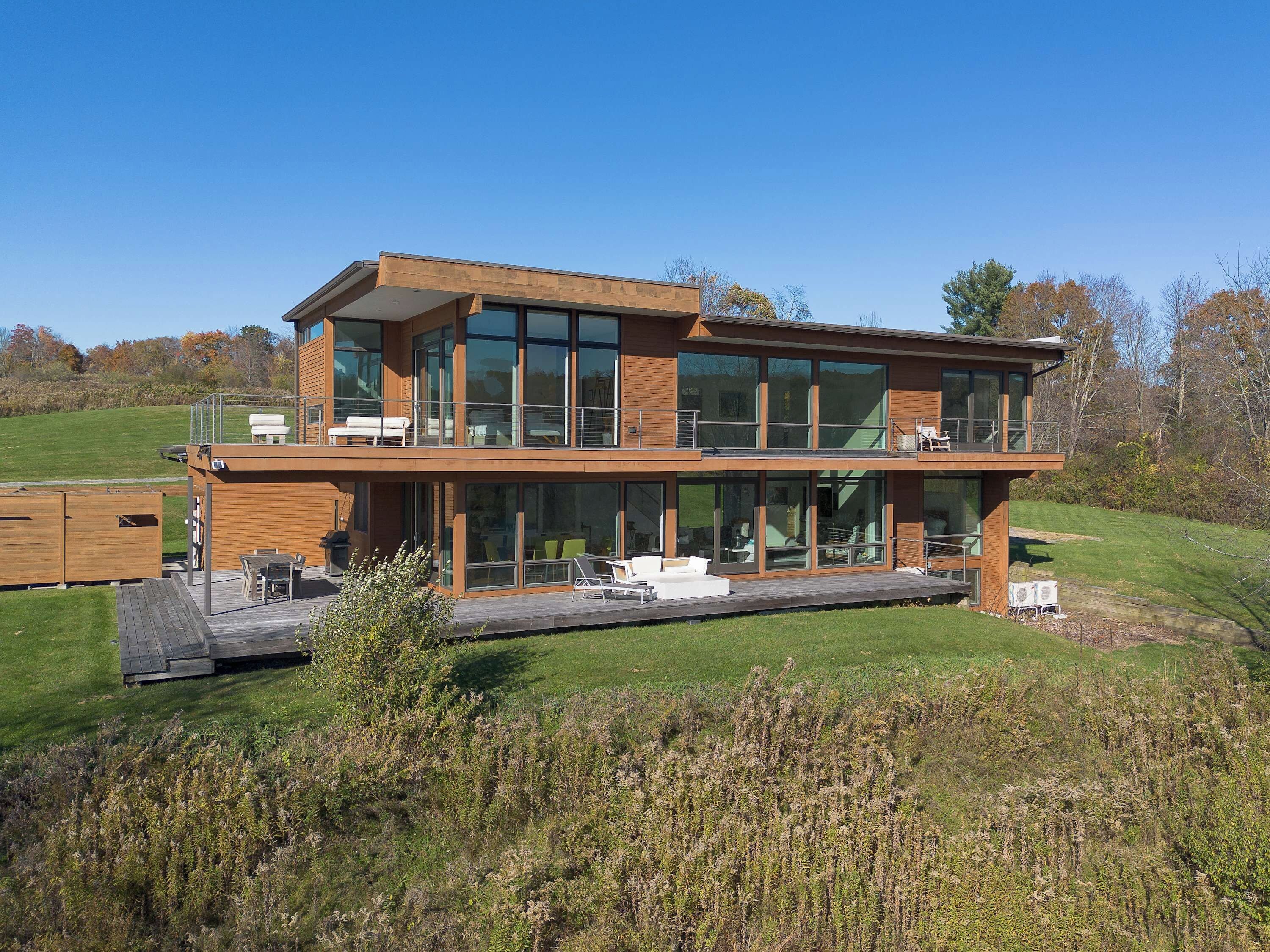 A modern two-story house with large windows, a deck, and outdoor furniture.