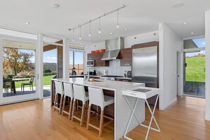 A modern kitchen with a central island, stainless steel appliances, and a view of a garden. - Hillsdale Lakeside | Modern Lakefront Retreat (Hillsdale)