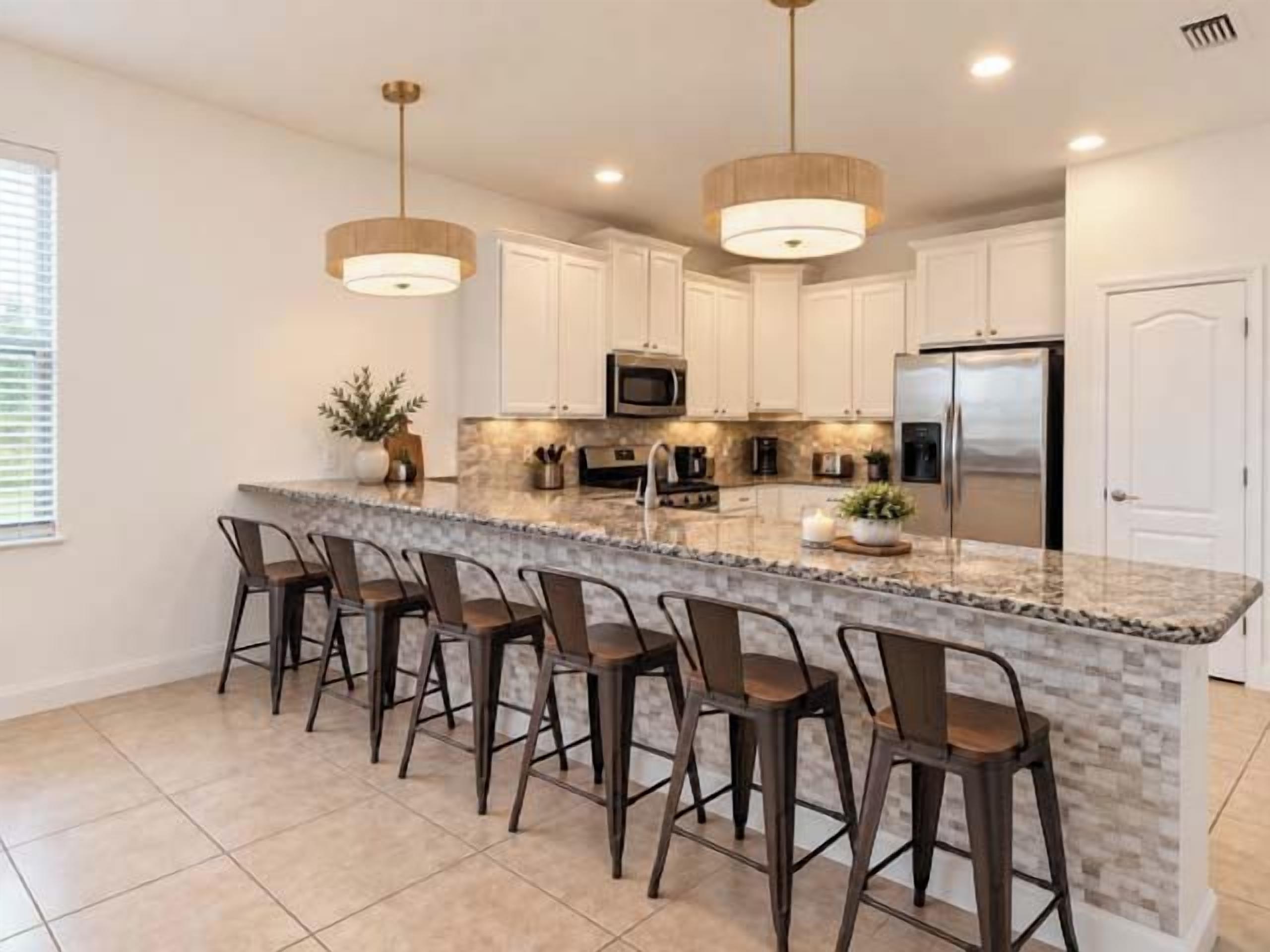 A kitchen with a central island, bar stools, white cabinets, stainless steel appliances, and pendant lighting.