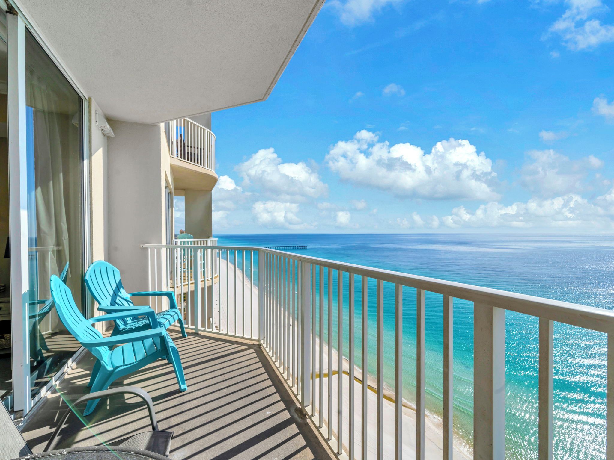 Un balcon avec des chaises turquoise, une vue sur l’océan et un ciel dégagé.