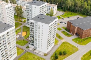 Un edifici residencial de grans alçades, amb múltiples balcons, una zona d'aparcament i un camp esportiu.